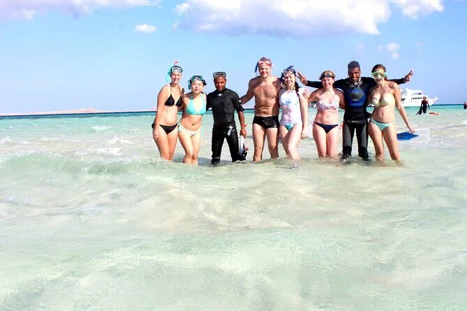 Group of eight tourists and two dive guides standing in shallow turquoise water wearing snorkel masks and fins