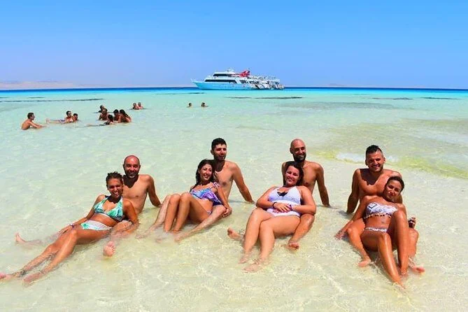 Deux couples détendus ensemble en eau turquoise peu profonde, un bateau de croisière blanc ancré en arrière-plan